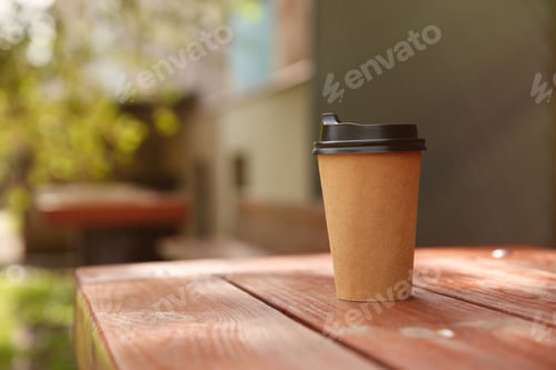 Preview: Takeaway paper coffee cup on wooden table outdoors, space for text