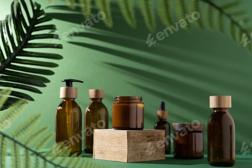 Preview: Bottles for cosmetics and cream on a pedestal, green background with leaves and shadow. Brown glass