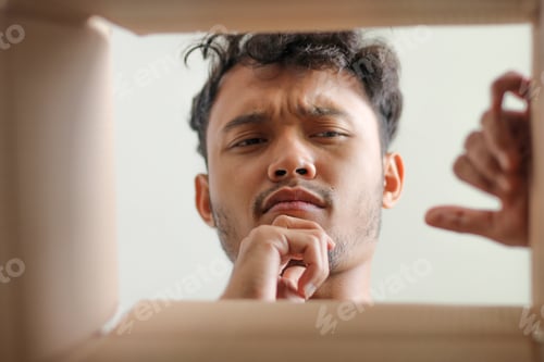 Preview: Young Asian Man Looking Into Box With Thoughtful Or Confused Expression Hands Reaching