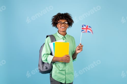 Preview: Happy african american teen exchange student with notebooks holding UK flag, smiling at camera on