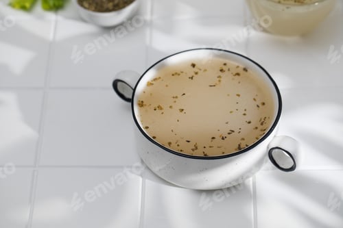 Preview: Healthy bone broth with spices on a white tile with a shadow pattern.