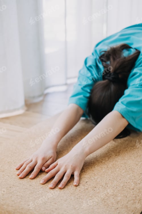 Preview: Close-up of a person stretching forward in childs pose on a cork yoga mat. Home yoga practice