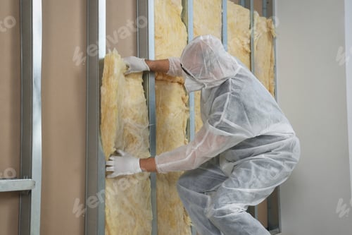 Preview: Worker in uniform and respiratory mask insulating wall indoors