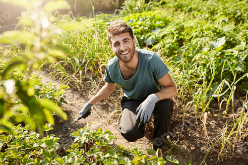 Preview: Young cheerful attractive bearded male gardener in blue t-shirt and black sport pants smiling