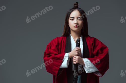 Preview: asian woman in kimono holding katana sword and looking at camera isolated on grey