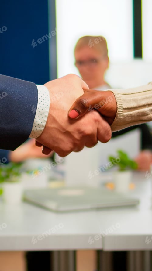 Preview: Close up of multiracial business partners standing in front of conference desk shaking hands