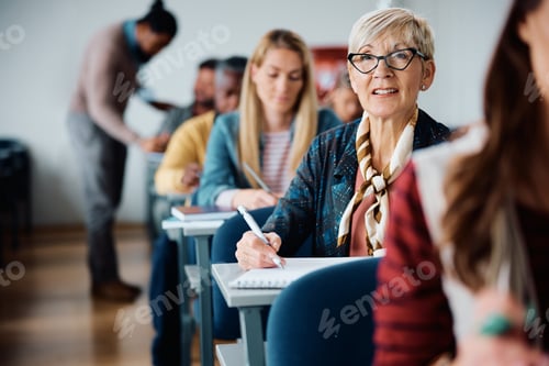 Preview: Mature female student taking notes while attending a course in lecture hall.