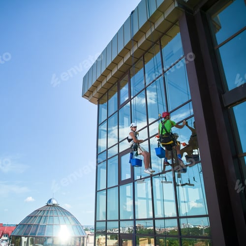 Preview: Industrial mountaineering worker cleaning window outside building.