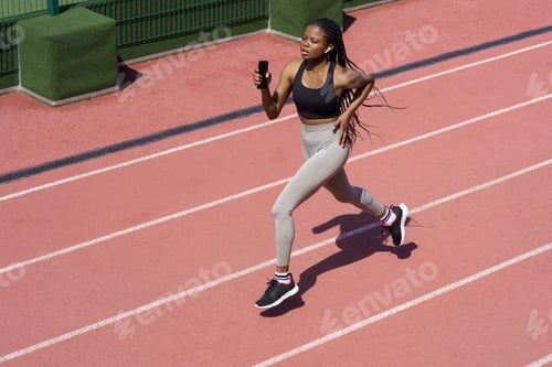 Preview: African woman athlete running on racetrack. Sportive black female training jog on stadium sprinting