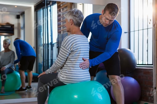 Preview: Physiotherapist assisting senior woman on exercise ball