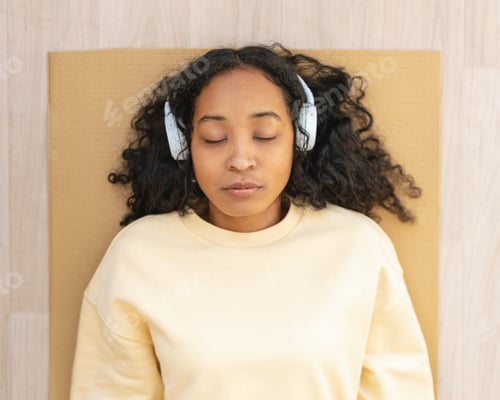 Preview: African-american woman in headphones resting on mat with closed eyes. Relaxing after exercising