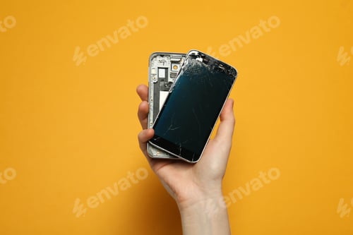 Preview: Woman holding damaged smartphone on orange background, closeup. Device repairing