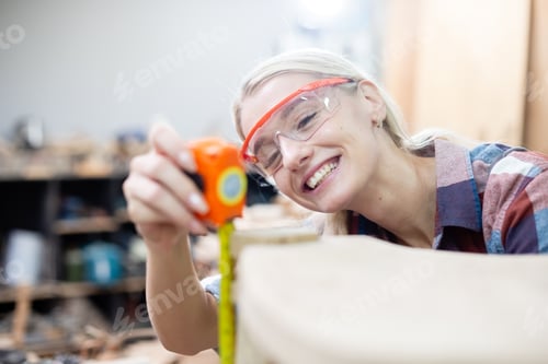 Preview: young carpenter women using measuring tape looking wood size at workspace.
