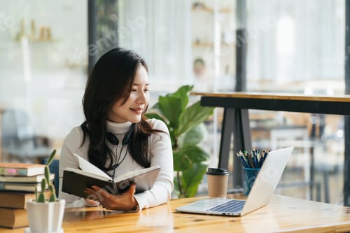 Preview: Head shot happy young asian female manager wearing headphones, looking at laptop screen, holding ple