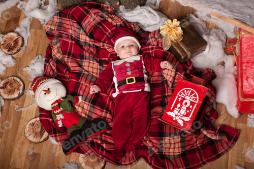 Preview: A child in Santa Claus costume rests on a red plaid surrounded by toys