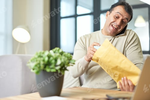 Preview: Multitasking. Portrait of hispanic middle aged business man talking on the phone while working from