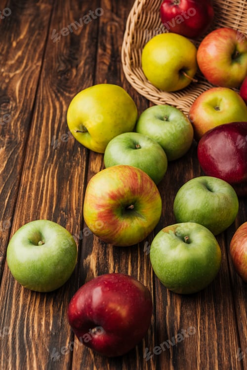 Preview: scattered multicolored apples and wicker basket on wooden table