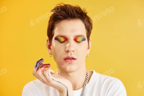Preview: Young gay man is standing in the studio and posing for a camera. Rainbow make up