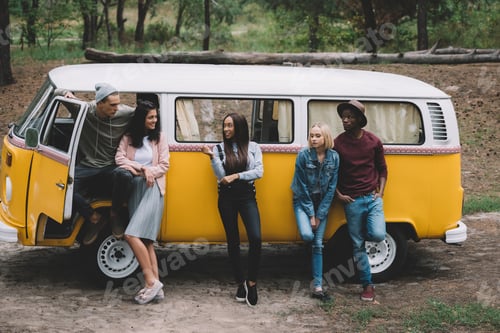 Preview: young multiethnic friends traveling together by retro minivan in forest