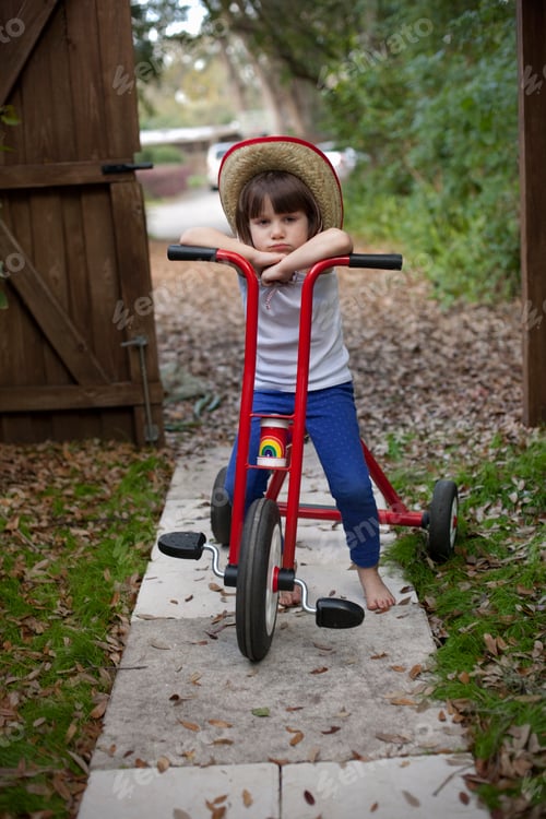 Preview: Portrait of four year old girl sitting on her tricycle in garden