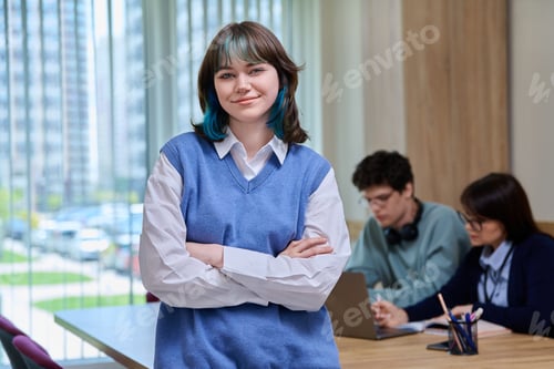 Preview: Smiling trendy female student looking at camera, posing in college classroom
