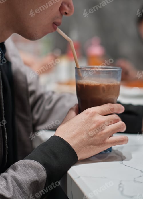 Preview: Vertical portrait of a young man drinking ice tea using a straw