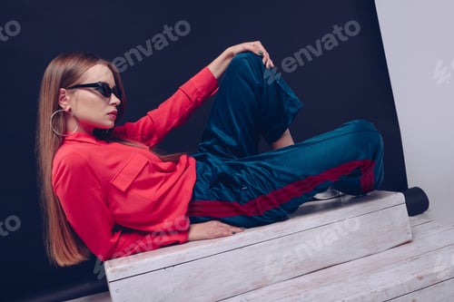 Vista previa: Stylish girl in red shirt and black sunglasses lying on a wooden stairs