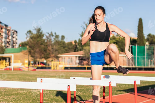Preview: athlete training by jumping hurdles on an athletics track.