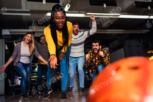 Preview: Group of friends enjoying time together laughing and cheering while bowling at club.