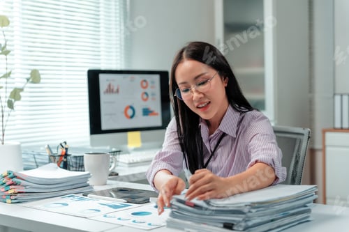 Preview: Asian businesswoman analyzing financial charts and working with documents in office