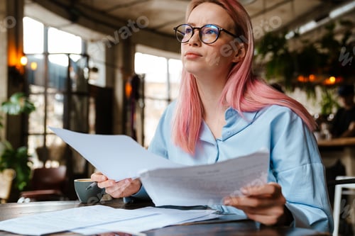 Preview: Young beautiful woman with pink hair doing paperwork in cafe