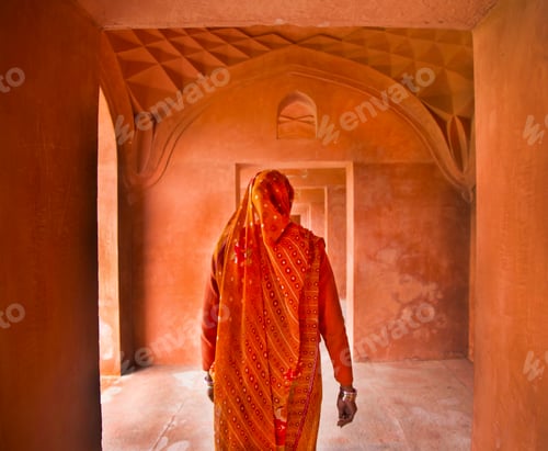 Preview: Rear view of woman wearing orange sari walking along passageway.
