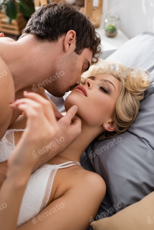 Preview: Sexy man touching chin of pretty blonde girlfriend in bra on bed