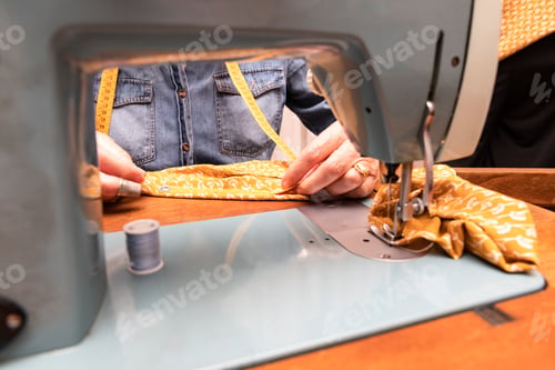 Preview: hands of older woman measuring an orange fabric with a tape measure on the wooden furniture