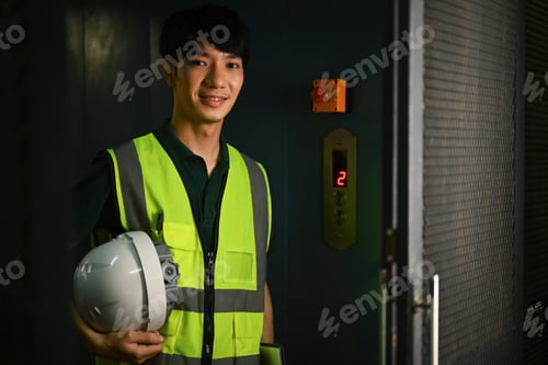 Preview: Portrait of male worker holding hardhat and smiling to camera while standing in industrial plant