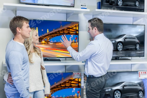 Preview: Shop assistant showing flatscreen TVs to young couple
