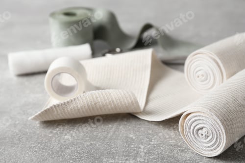 Preview: Medical bandage rolls and sticking plaster on grey table, closeup