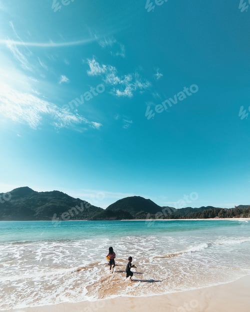 Preview: Beautiful landscape view of two kids playing in water beach with mountains with a sunny blue sky