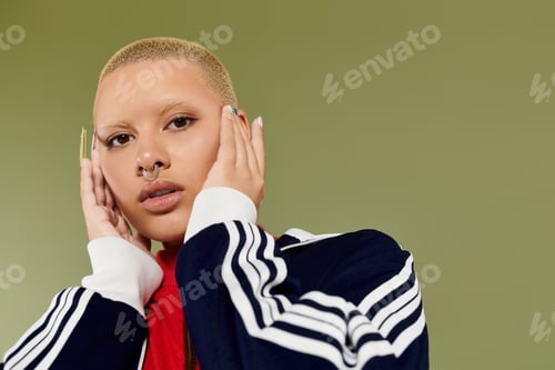 Preview: A stylish young bald woman wearing vibrant attire poses thoughtfully against a green backdrop