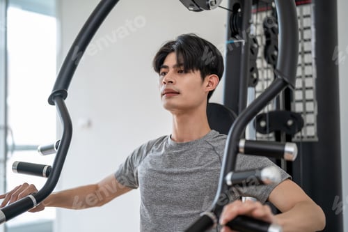 Preview: Asian young sportsman exercise by lift up weight machine in gym stadium.