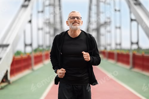 Preview: Cheerful athletic senior man running by bridge