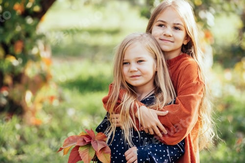 Preview: portrait of two happy sisters laughing hugging each other on warm and sunny summer day in garden