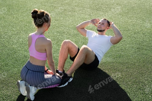 Preview: Man and a woman pump their abs in the park on the grass.