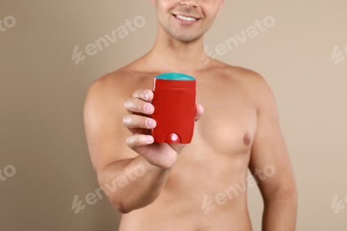 Preview: Young man holding deodorant on beige background, closeup. Mockup for design