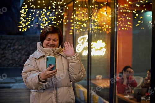 Preview: Woman in the Light winter jacket is talking by the phone next to the Christmas decorated cafe