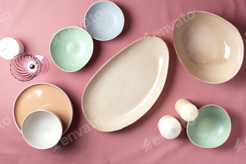 Preview: Light pastel colored tableware set: empty serving plates, bowls, candles on pink shabby background