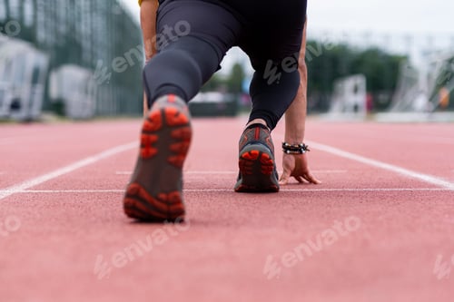 Preview: Close-up view of runner legs in a low start position beginning of sprint along urban outdoor stadium