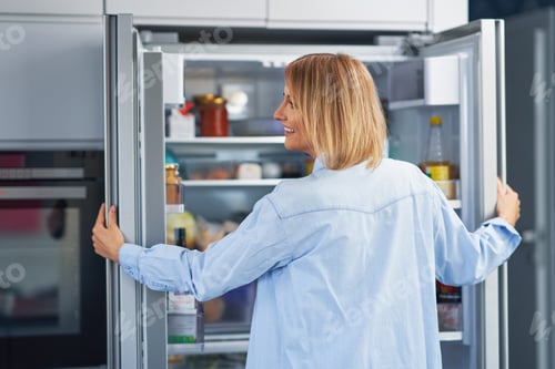 Preview: Young adult woman in the kitchen with the fridge