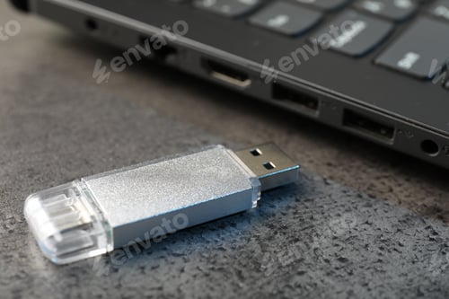 Preview: USB flash drive and laptop on dark grey table, closeup