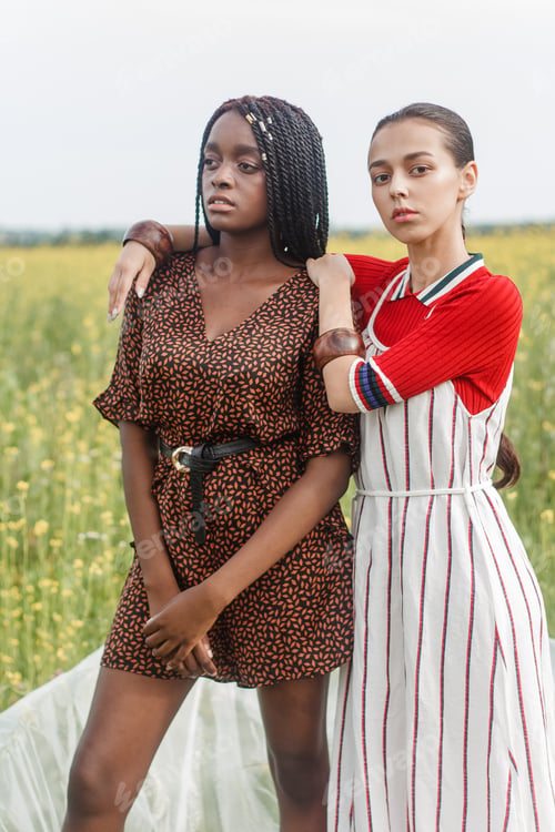 Preview: Black and white girls are standing opposite each other in a field with yellow flowers.